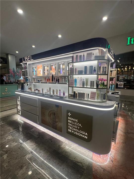 Isla de belleza con muebles curvos y repisas iluminadas en centro comercial
